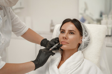 Cosmetologist makes injections to increase lips and anti-wrinkles of woman in beauty salon