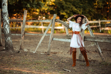 portrait of a beautiful young woman in a white dress with over the knee boots and a hat with a belt...