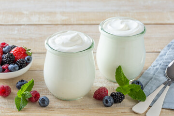 fresh greek yogurt in glass jar served with mixed berries, healthy breakfast concept, wooden background