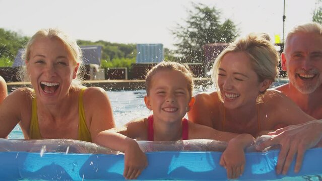 Portrait of smiling multi-generation family on summer holiday relaxing floating on inflatable airbed and splashing in swimming pool - shot in slow motion