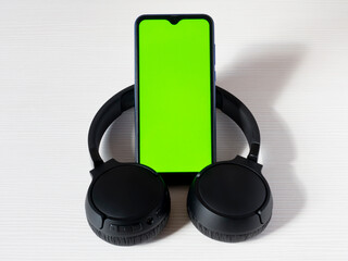 A mobile phone with a green screen for editing blanks is installed inside large black headphones on...