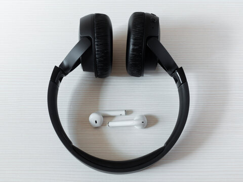 Beneath the large black earpieces lies a pair of portable earphones, small and large earphones, sound and size.