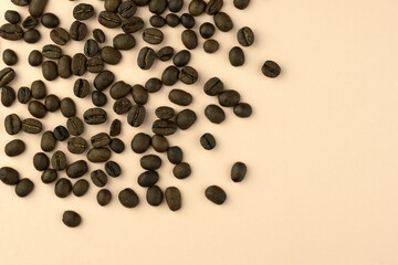 Roasted black coffee beans scattered on a light background, close-up.
