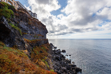 Seascape with blue sky, smooth water surface and rocky cliffs covered with grass