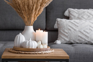 Still-life. Dried pampas grass in a vase, white ceramic pumpkins, a teapot, a cup and pumpkin-shaped candles on a coffee table in the home interior of the living room. Cozy autumn concept.