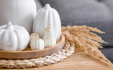 Still-life. White ceramic pumpkins, pampas grass, pumpkin-shaped candles on the coffee table in the...
