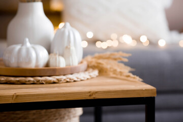 Fototapeta na wymiar Still-life. White ceramic pumpkins, pampas grass, pumpkin-shaped candles on the coffee table in the home interior of the living room. Details of the decor. Cozy autumn concept.