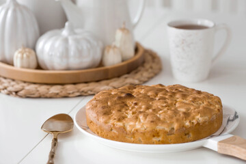 Still-life. Dried pampas grass in a vase, white ceramic pumpkins, candles and apple pie charlotte on a white table in the interior of a Scandinavian-style home kitchen. Cozy autumn concept.