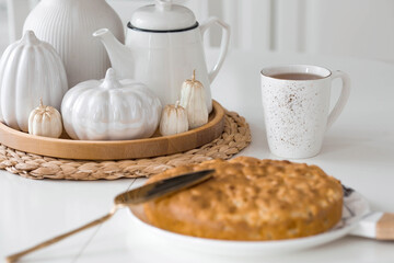 Still-life. Dried pampas grass in a vase, white ceramic pumpkins, candles and apple pie charlotte on a white table in the interior of a Scandinavian-style home kitchen. Cozy autumn concept.