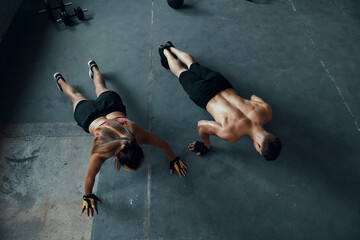 Top view of young fit couple doing push-ups in gym together