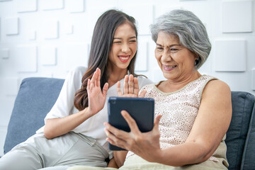 Asian woman, elderly, mother and daughter using smartphone for video call with happy mood smiling and laughing on sofa at home.