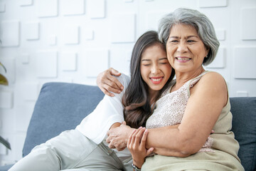 Asian grandma and granddaughter hugged with happy mood on the sofa in home.