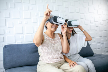 Asian grandmother and granddaughter using virtual reality play games at home. Senior and young woman wearing VR-headset glasses on sofa in living room.