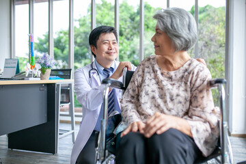 Asian doctor supporting and cheering up senior patient in wheelchair talking, smiling in comfort at home. Healthcare and medicine concept.