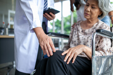 Asian doctor checking knee of elderly patient on wheelchair, healthcare and medical concept.