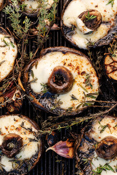 Grilled portobello mushrooms with melted mozzarella cheese and herbs on a cast iron grill plate, close up view