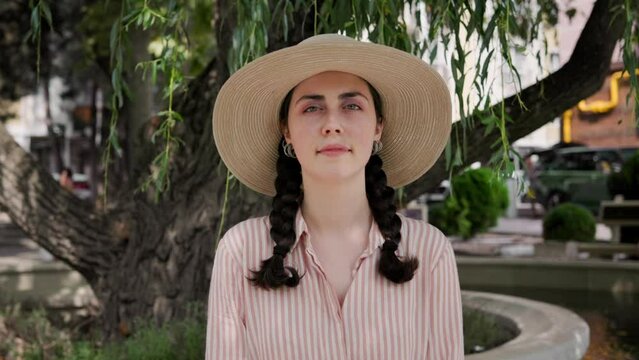 Portrait of sad beautiful young woman in a straw hat posing at park. Concept of summer vacation and psychology.