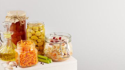 Fototapeta na wymiar Autumn seasonal pickled or fermented vegetables, mushrooms and olive oil in glass jars on a white wooden board on a light neutral background with copy space. Fall home food preserving or canning