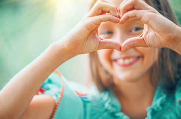 Cute child, happy little girl showing heart gesture and smiling outdoor. Love summer. Beautiful seven years old child enjoying nature outdoors. Healthy carefree kid playing outside in a park. Love