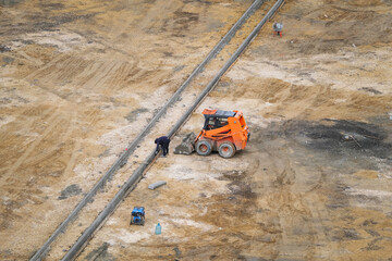 Worker laying concrete curbs next to excavator at construction site, top view