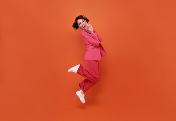 Fototapeta na wymiar Happy beautiful woman smiling and jumping while celebrating success isolated over orange background.