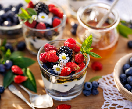 Dessert of various berries and natural yoghurt with addition honey, fresh mint and edible daisy flowers, close-up.  Healthy and delicious breakfast.
