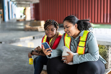 Two female African workers take a break, sitting and watching on mobile phone. chatting, sending...
