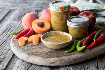 Jars of peach and peppers salsa surrounded by ingredients used to make it. 
