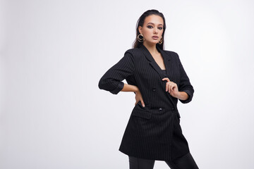 Fashion photo of a beautiful elegant young woman in a pretty black jacket, leather pants, boots, posing over white background. The hair is gathered back, dark brunette. Studio Shot