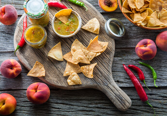 Peach and pepper salsa served with tortilla chips on a rustic wooden board.