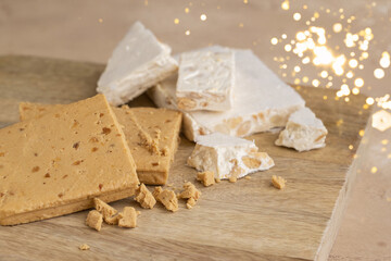 Artisan hard and soft Nougat, made with almonds and honey on wooden cut board with gold boke....