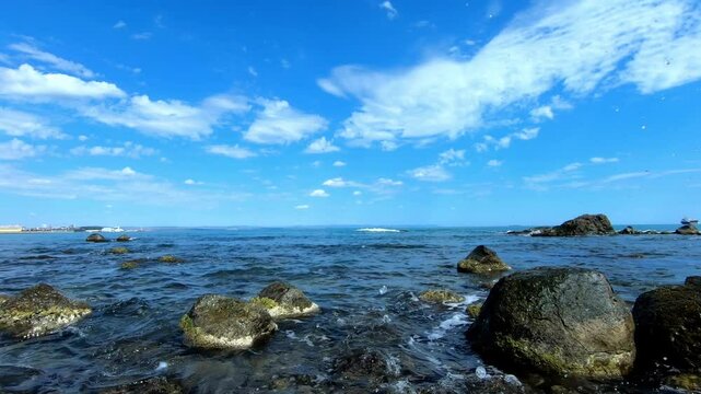 stony shore of the black sea from Cape Foros in Kraymorie Bulgaria. Burgas port in background. Cargo ship, small waves, few stones, blue sky, clouds