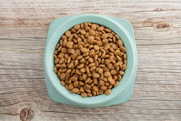 Dry food for cats and dogs in a green bowl on a wooden background.