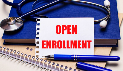 On the table are notepads, a stethoscope, a pen and a sheet of paper with the text OPEN ENROLLMENT....