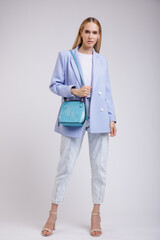 High fashion photo of a beautiful elegant young woman in a pretty jacket, blazer, denim jeans, aqua blue handbag posing over white, soft gray background. Studio Shot.