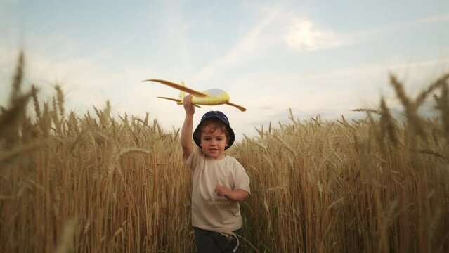 cute baby boy with toy plane in hand running in golden rye field, portrait of happy carefree child