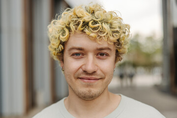 Close-up smiling young caucasian man with tattoos on his face smiling for camera. Curly blonde guy wears earring in ear. Concept fashion, portrait.