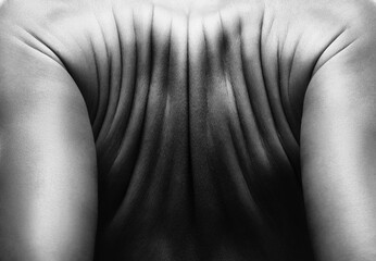 Wrinkled back of a woman close-up in black and white. A woman does an exercise for back pain.