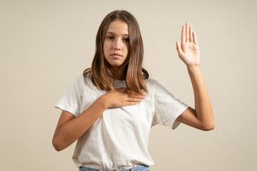 Young brunette hispanic teenager standing together over isolated beige background swearing with hand on chest and open palm, making a loyalty promise oath. - obrazy, fototapety, plakaty