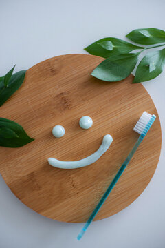 Smiling face made of toothpaste, brush on wooden background with green leaves, flat lay. High quality photo