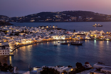Elevated view of Mykonos island with the old harbour, the famous windmills above and old town during summer dusk time, Cyclades, Greece - obrazy, fototapety, plakaty