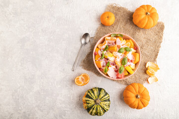 Obraz na płótnie Canvas Vegetarian fruit salad of yogurt pumpkin, tangerine, basil microgreen on gray, top view, copy space.