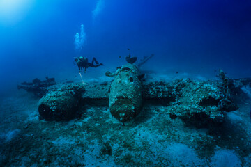 A scuba diver explores a sunken world war two fighter propeller airplane at the seabed of the...