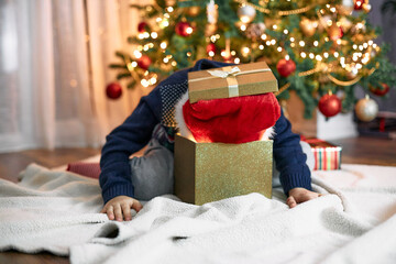 Funny boy in a santa claus hat stuck his head in a gift box. Funny kids. New Year's and Christmas