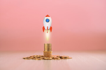 Rocket launching from the gold coin for business success and investment income or saving wealth management on the pink background in the office, Business startup concept.