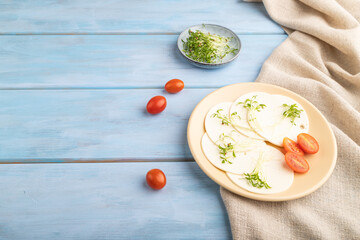 White cheese with tomatoes and cilantro microgreen on blue. side view, copy space.