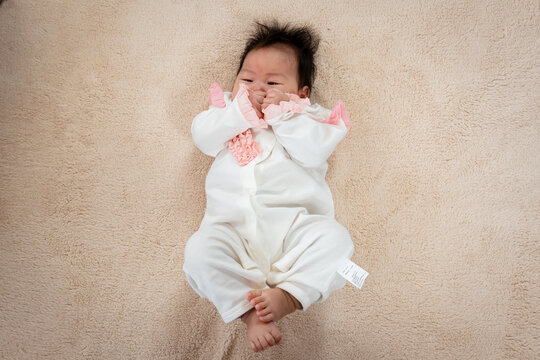 Newborn Asian girl lying in white on the bed just waking up from sleep. waiting for her mother to take care of her The little boy rolled around on the light brown bed.