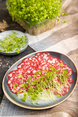 Slices of smoked cervelat salami sausage with spinach microgreen on black, side view, selective focus.