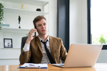 Obraz premium Businessman in suit talking on smartphone while working with laptop in office