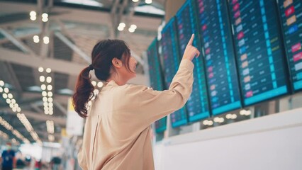 Happy asian woman traveler checking flight schedule board in airport terminal. Tourist journey trip concept
